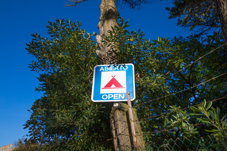 blue rectangular sign of camping open, in a trunk tree, in spanish and english, in Spain, Europeの写真素材