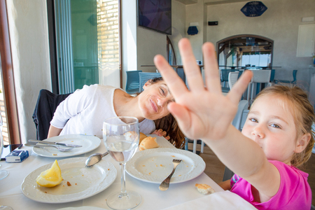 little girl four years old hiding with hand, or covering view, shutting out refusal. eating in restaurant with her mother, sitting in restaurant. Private life and paparazzi concept.の写真素材