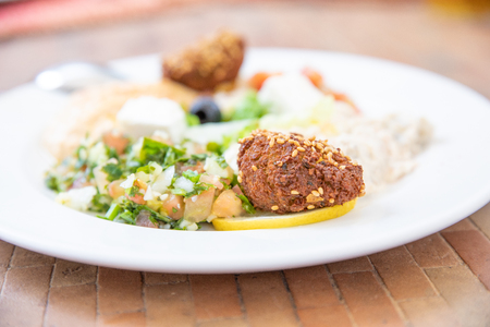 falafel (fried ball with chickpeas or fava beans) in white dish with mezze or meze, selection of typical Arabic appetizers (hummus, baba ghanoush, Feta cheese, Marrakesh salad, tabule, olives)の写真素材
