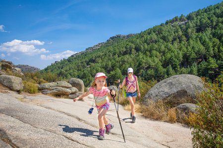 mountaineers family girl empower: woman and five years old girl, with caps, binoculars and trekking sticks, hiking in rocky mountain of Camorza Gorge (Madrid, Spain, Europe)の写真素材