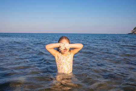 little girl with swimsuit in the water of Mediterranean sea covering her eyes with hands to protect herself from the sun, in Cabo de Gata Natural Park (Almeria, Andalusia, Spain)の写真素材