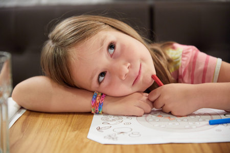 Six years cute blonde girl with her head resting on her arm imagining what to draw on a sheet of...