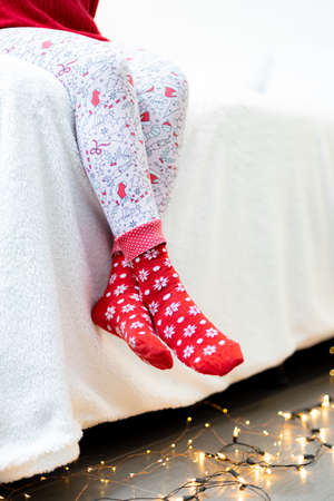 Woman wearing red Christmas socks sitting on the bed with garland.の写真素材