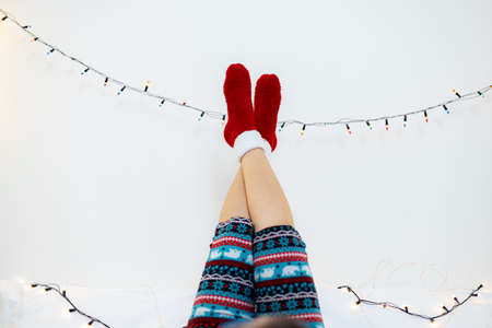 Female legs in warm knitted socks with Christmas lights on a white backgroundの写真素材