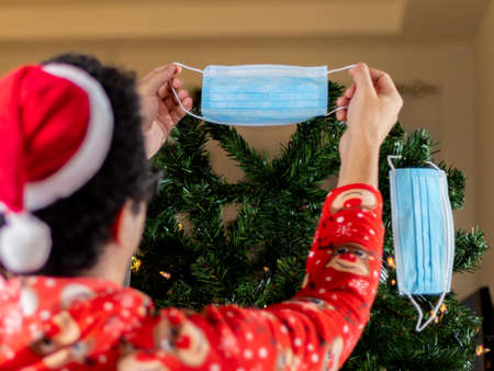 Christmas and New Year concept. A man in Santa Claus clothes puts on a medical mask on the Christmas tree.の写真素材
