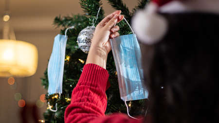 Young woman in red sweater and Santa hat decorating christmas tree with medical masks.の写真素材