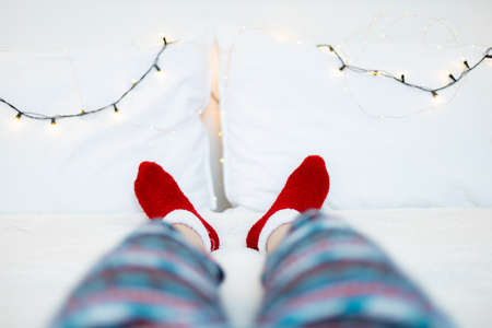 Female legs in red socks on the bed with Christmas lights garlandの写真素材