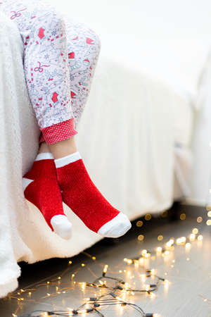 Little girl in christmas socks sitting on the bed with garlandの写真素材