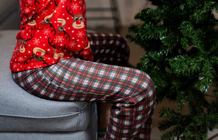 A girl in pajamas sits on a chair near the Christmas tree.の写真素材