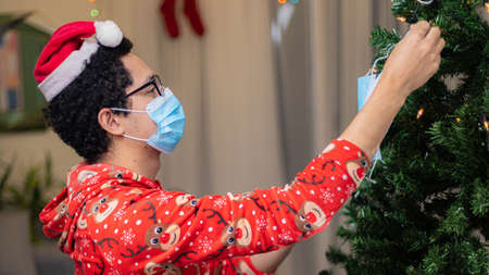 A man in a medical mask and a red suit is decorating a Christmas tree.の写真素材