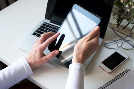 A business woman's hands using tablet with smart phone, glasses and notebook and coffee on white...