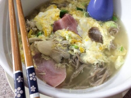 Asian style soup with chopsticks on bowl of egg ham mushroomの写真素材