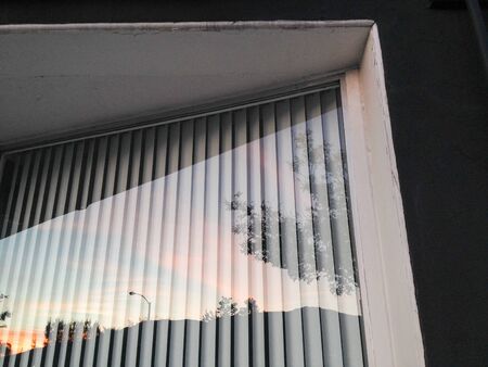 Glass window reflection of sunset with vertical blinds and mountain horizon cloudsの写真素材