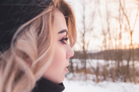Young blonde girl in black clothes looking at the distant winter sunset