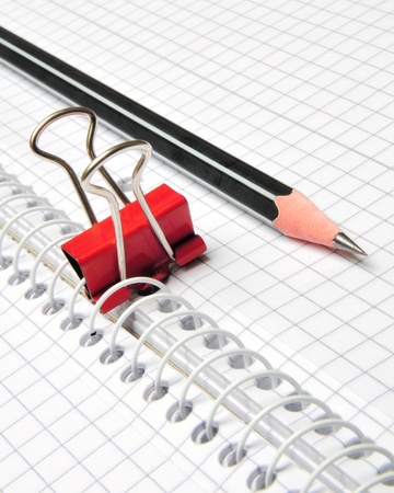 Black pencil on top of a notepad with squared paper an red clip の写真素材