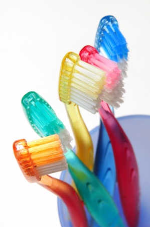 Five colorful toothbrushes in a blue glass on white background の写真素材