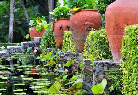 Red terracotta pottery between green plants and hedges above a water ditch の写真素材