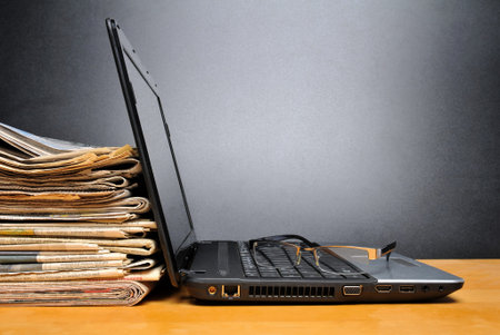 Laptop and newspapers on a table with black backgroundの写真素材