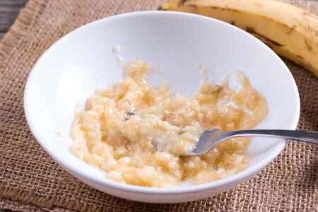 Slices of banana in a bowl and fork on the tableの写真素材