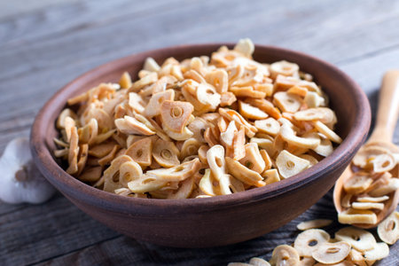 Bowl with dried garlic flakes on wooden tableの写真素材