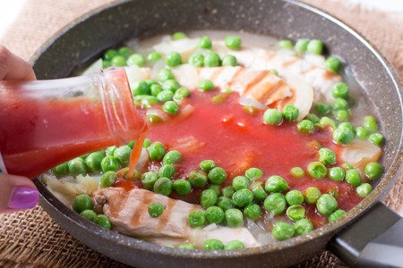 Chicken fillet, onion, peas and tomato sauce in a frying panの写真素材