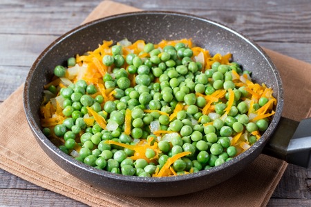 Peas, onions and carrots on a frying pan on a tableの写真素材