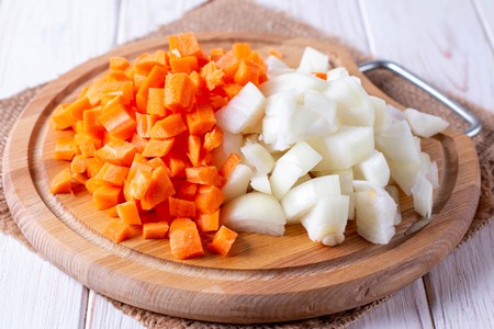 Onions and carrots chopped on a cutting board on a wooden table, horizontalの写真素材