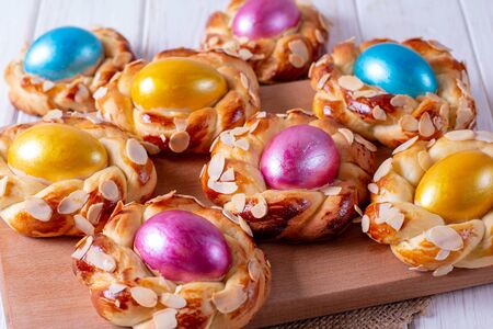 Homemade sweet Italian Easter Bread Rings with dyed eggs on an old white wooden table, view from above, close-upの写真素材