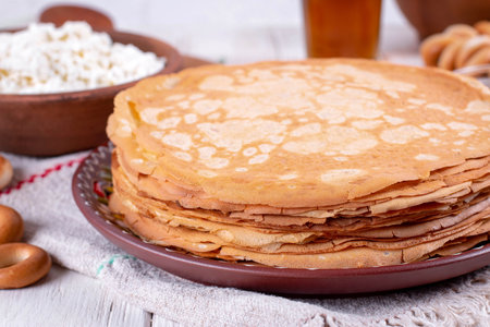 Stack of thin pancakes in a plate on a white wooden table