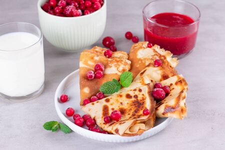 Thin pancakes or crepes on a plate with jam and frozen berries, mint. Traditional breakfast or dessert.の写真素材