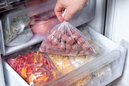 Man putting plastic bag with meatballs in refrigerator with frozen vegetables, closeupの写真素材