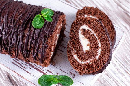Delicious chocolate roll sponge cake with vanilla cream and mint leaves. Desert sweet food
