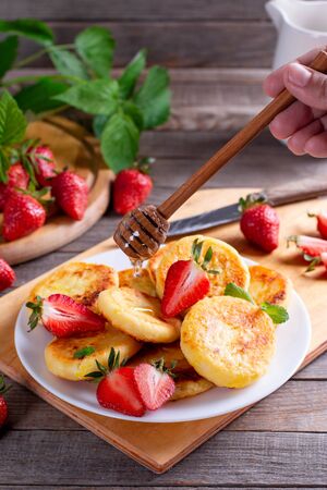 Cottage cheese pancakes with strawberry on a white plate on a wooden table. Breakfast or Lunch Concept.の写真素材
