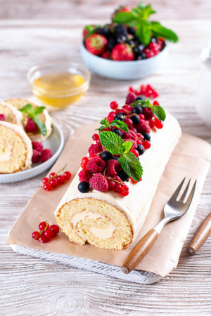 Sponge cake roll filling cream and berries, strawberry, raspberries, blueberry and red currants on white wooden background. Soft focus. Summer food conceptのeditorial素材