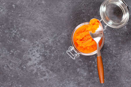 Carrot jam with orange in a glass jar on a dark concrete background. Vegetable jams. Preservation, copy spaceの写真素材