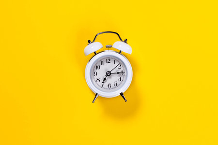 White small alarm clock on yellow background. Top view.