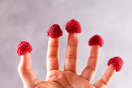 Ripe large raspberries are dressed on the fingers of the hands. Like funny hats. Hand with berries...