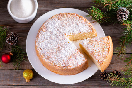Homemade sponge cake with powdered sugar on a white plate on a wooden table. New Year and Christmas...
