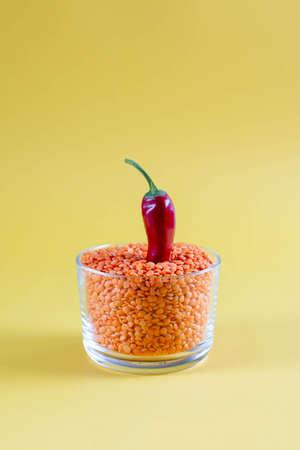 Red lentils in a glass jar with red chili peppers on a yellow background. Healthy food concept, color trend, food wallpaperの写真素材