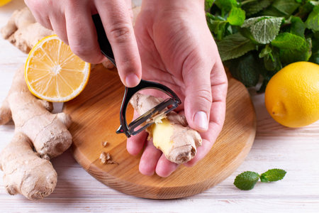 Man hands peeling fresh ginger root with knife on wood board