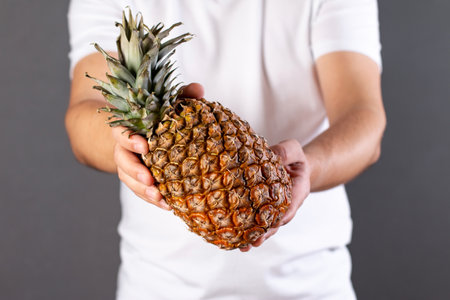 Young man holding a ripe and juicy pineapple. Appropriate healthy nutrition, vitamin concept, soft focusの写真素材