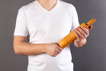 Man holds rolling pin in hand, standing against gray background. Place for text. Copy spaceの写真素材