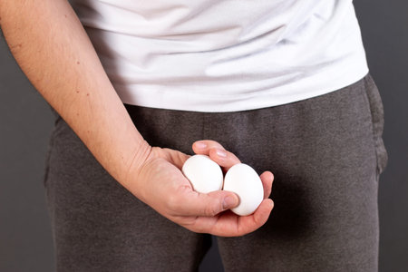 Man hands holding eggs on middle crotch of trousers isolated on gray background