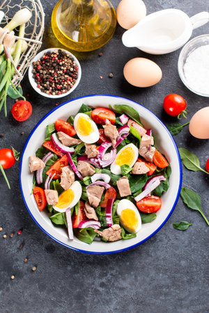 Salad with canned fish, eggs, spinach and tomato on a white plateの写真素材
