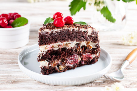 Chocolate layered sponge cake with cherries on a plate on a wooden table