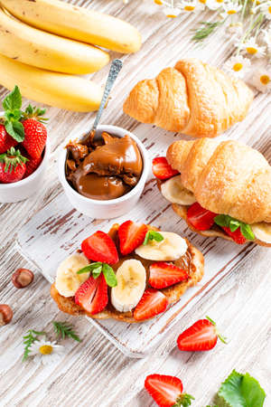 Croissant Sandwich with banana, chocolate and strawberry on wooden table. Delicious breakfast. Top viewの写真素材