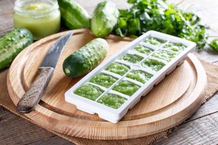 Frozen cucumber puree in ice cube trays ready for freezing on a cutting board on a wooden table. Frozen Food Concept.の写真素材