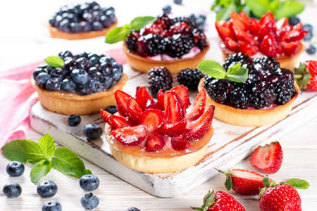 Strawberries, blueberries, blackberries tartlets with chocolate ganache, fresh berries and mint leaves, selective focus. Fresh fruit tart, freshly homemade fruit cake on a tableの写真素材