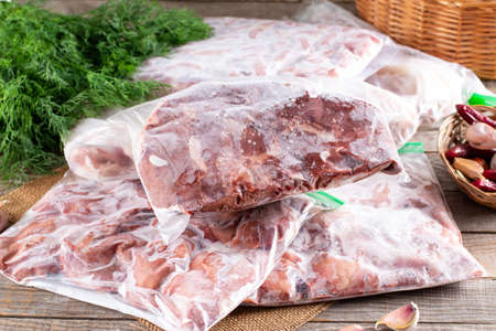 Frozen meat. Frozen offal, liver, heart, stomachs in a plastic bag on a wooden table. Frozen products. Frozen foodの写真素材