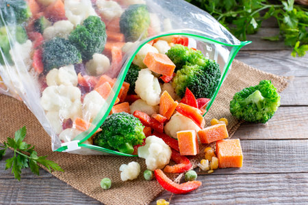 Plastic bags with different frozen vegetables on a wooden table. Food storageの写真素材